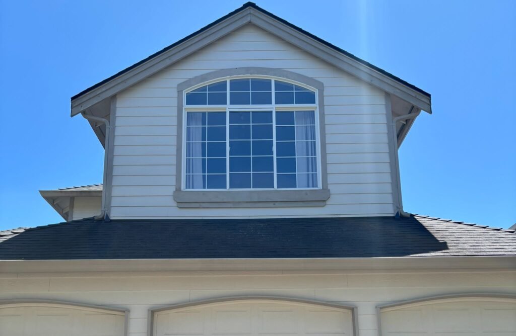 Close-up view of a house with a large window and sloped roof under a clear blue sky