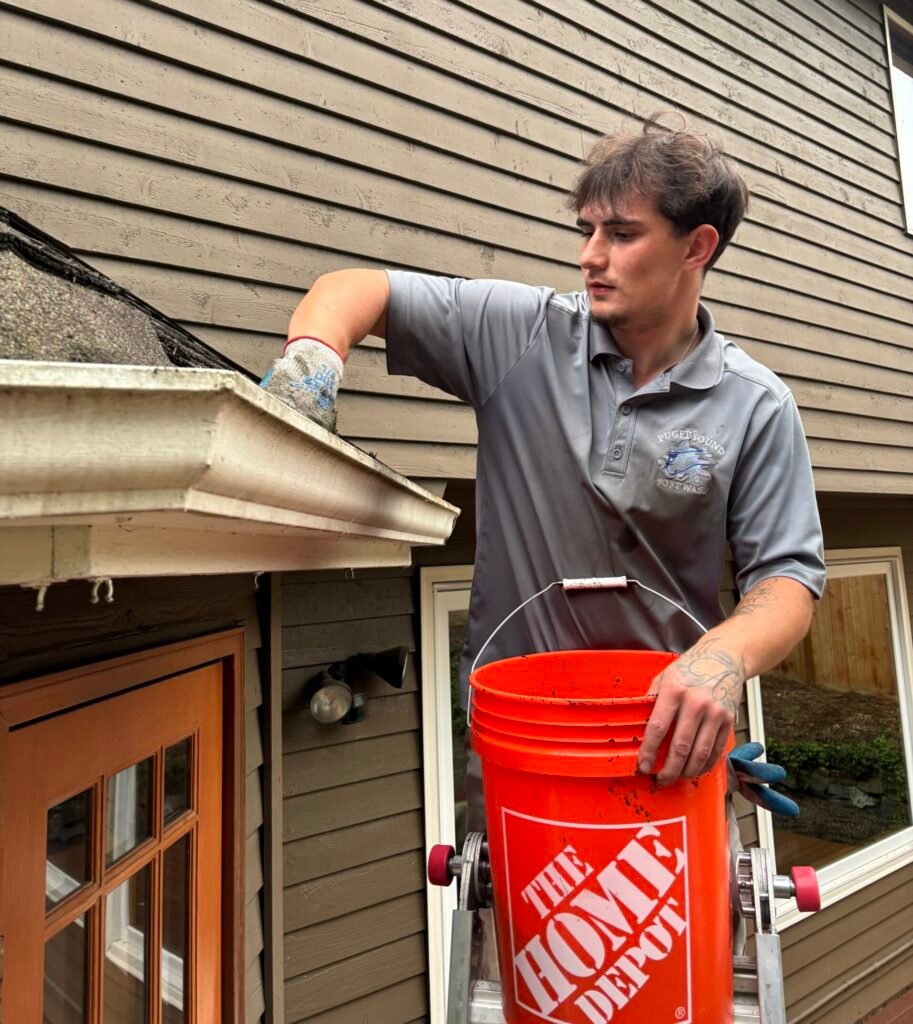 Person cleaning gutters using a glove, with a Home Depot bucket placed on a ladder
