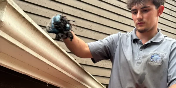 Person cleaning gutters on a wooden house, holding debris with a gloved hand
